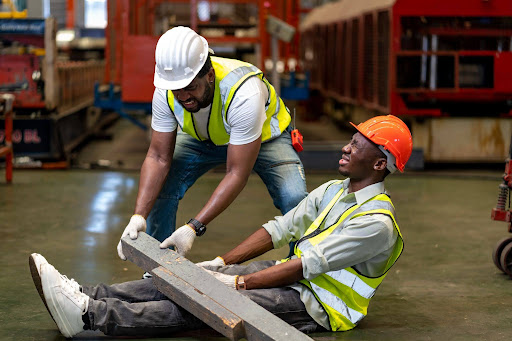 A factory worker helps another worker remove a steel beam which fell on him before writing an incident report